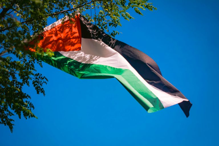 Vibrant Palestinian flag waving against a clear blue sky, representing freedom and patriotism.